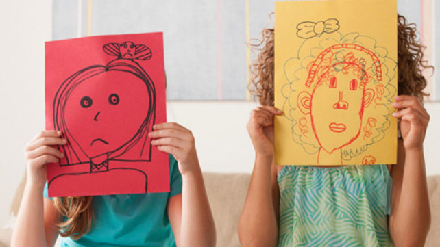Children holding drawings in front of their faces