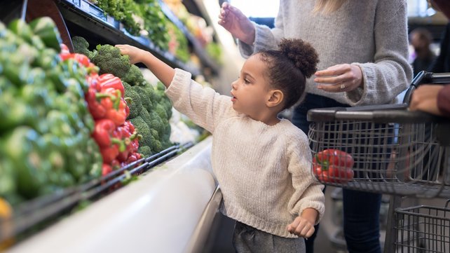 young child in grocery store picking out vegetables to put in shopping cart