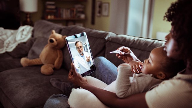 Woman holding baby on her lap and participating in a telemedicine visit from her living room